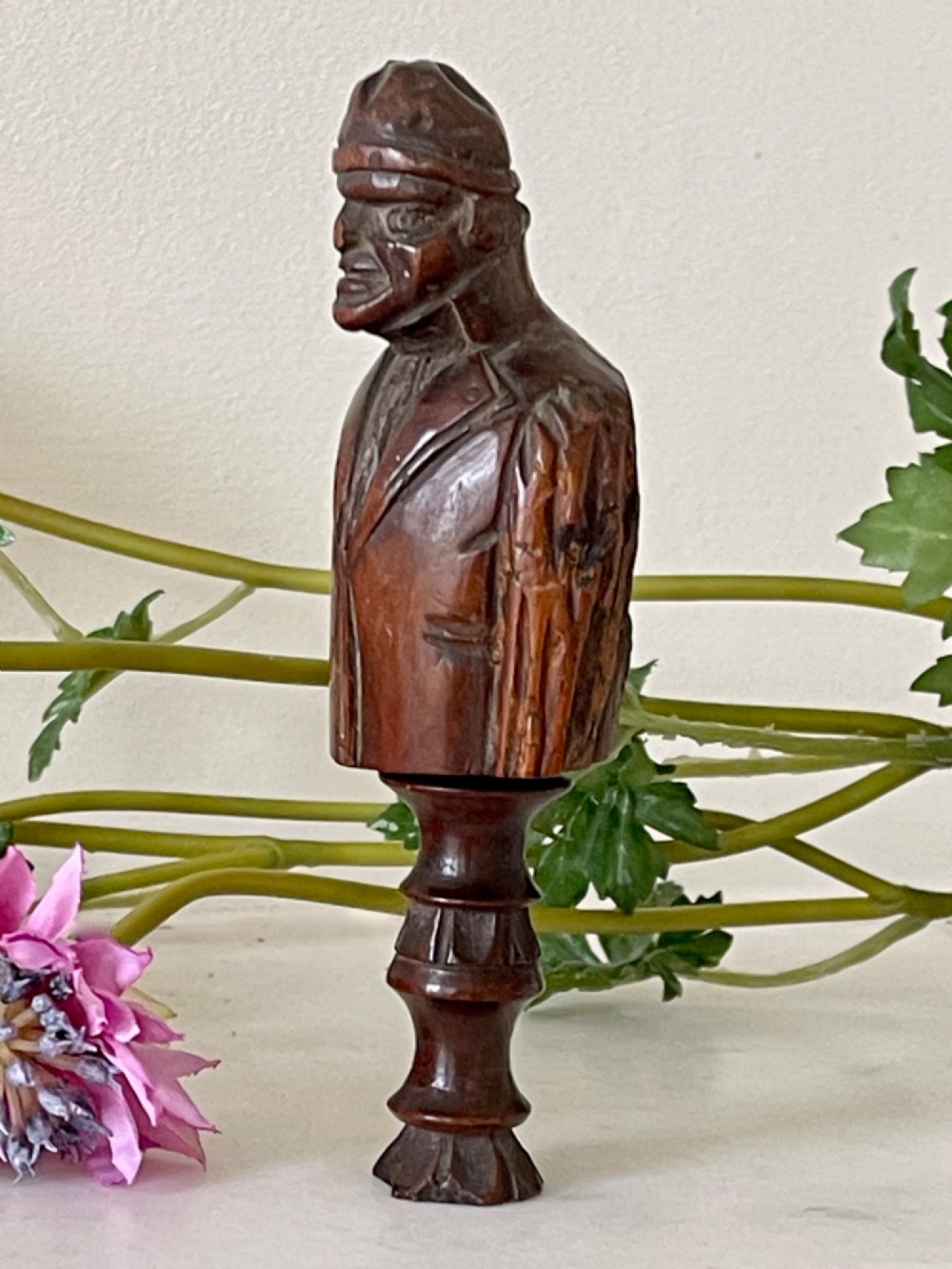 A dark carved wooden treen nutcracker featuring a male bust wearing a cap and jacket atop a turned pedestal handle. View IV