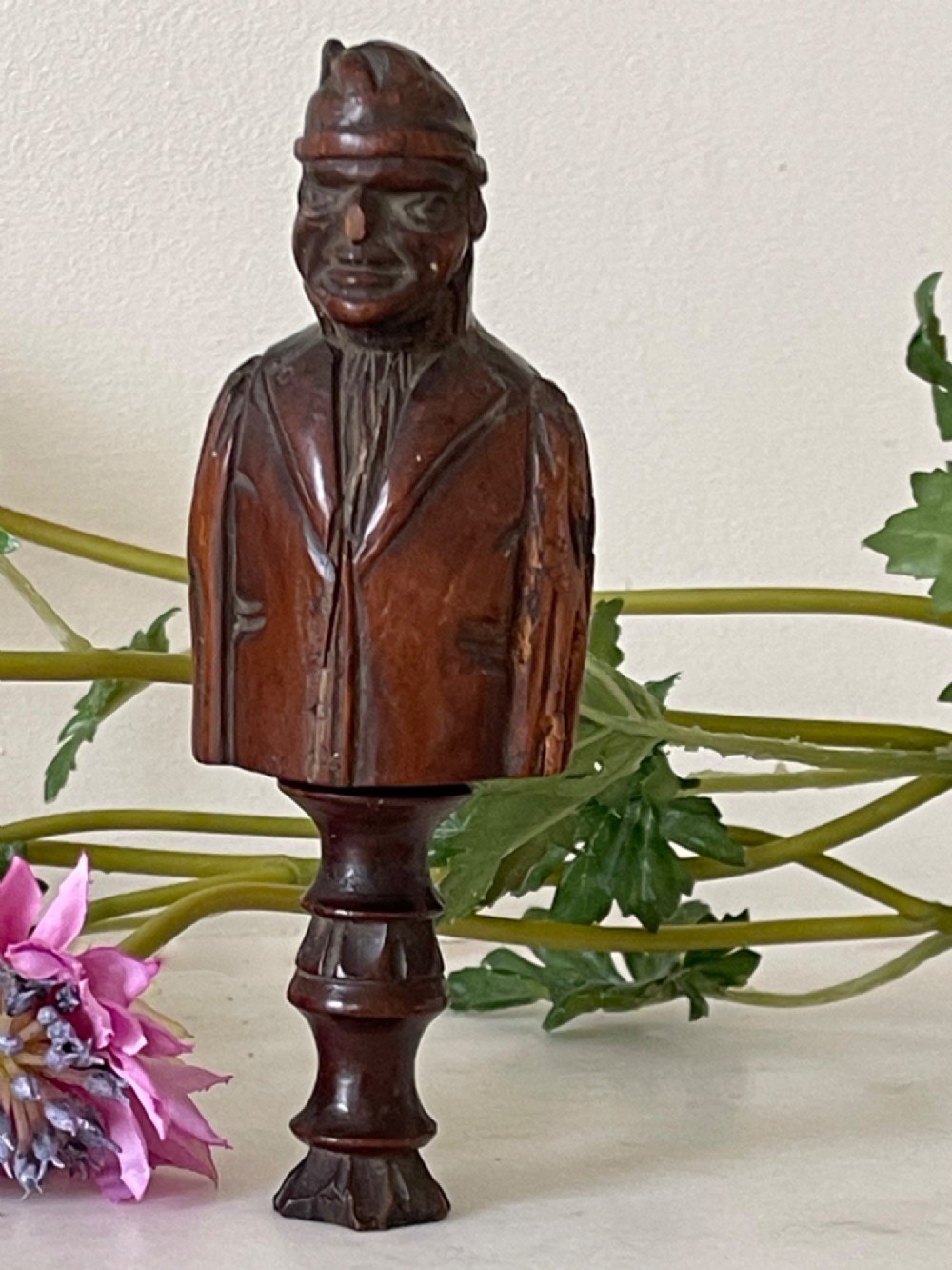 A dark carved wooden treen nutcracker featuring a male bust wearing a cap and jacket atop a turned pedestal handle. View VI