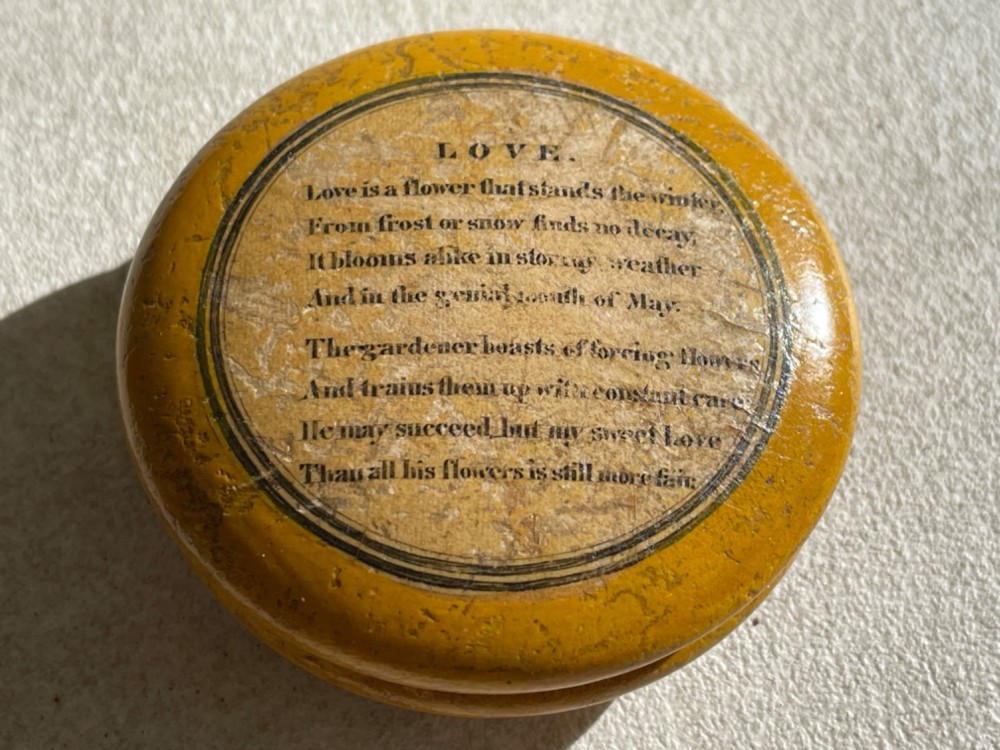 A circular yellow wooden antique Scottish snuff box with a printed love poem on the top lid.