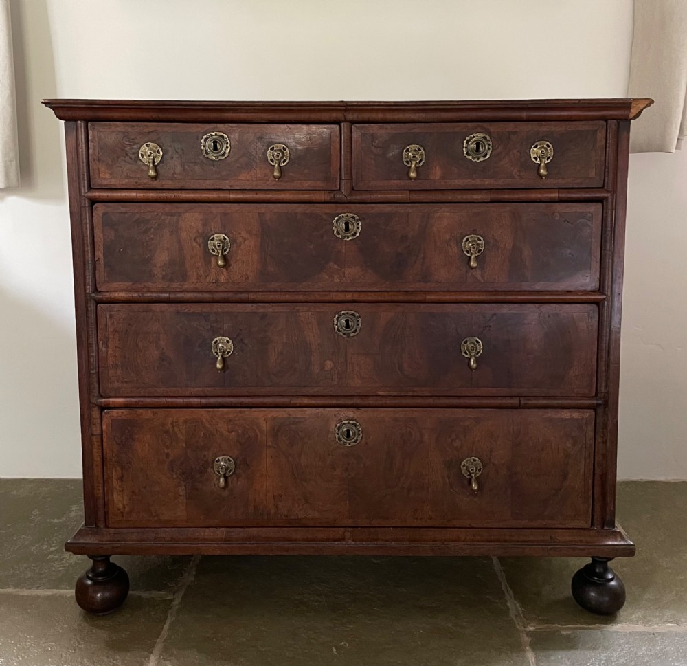 A late 17th-century walnut chest of drawers featuring brass teardrop handles, keyhole escutcheons, crossbanded veneer drawer fronts, and turned bun feet. View II