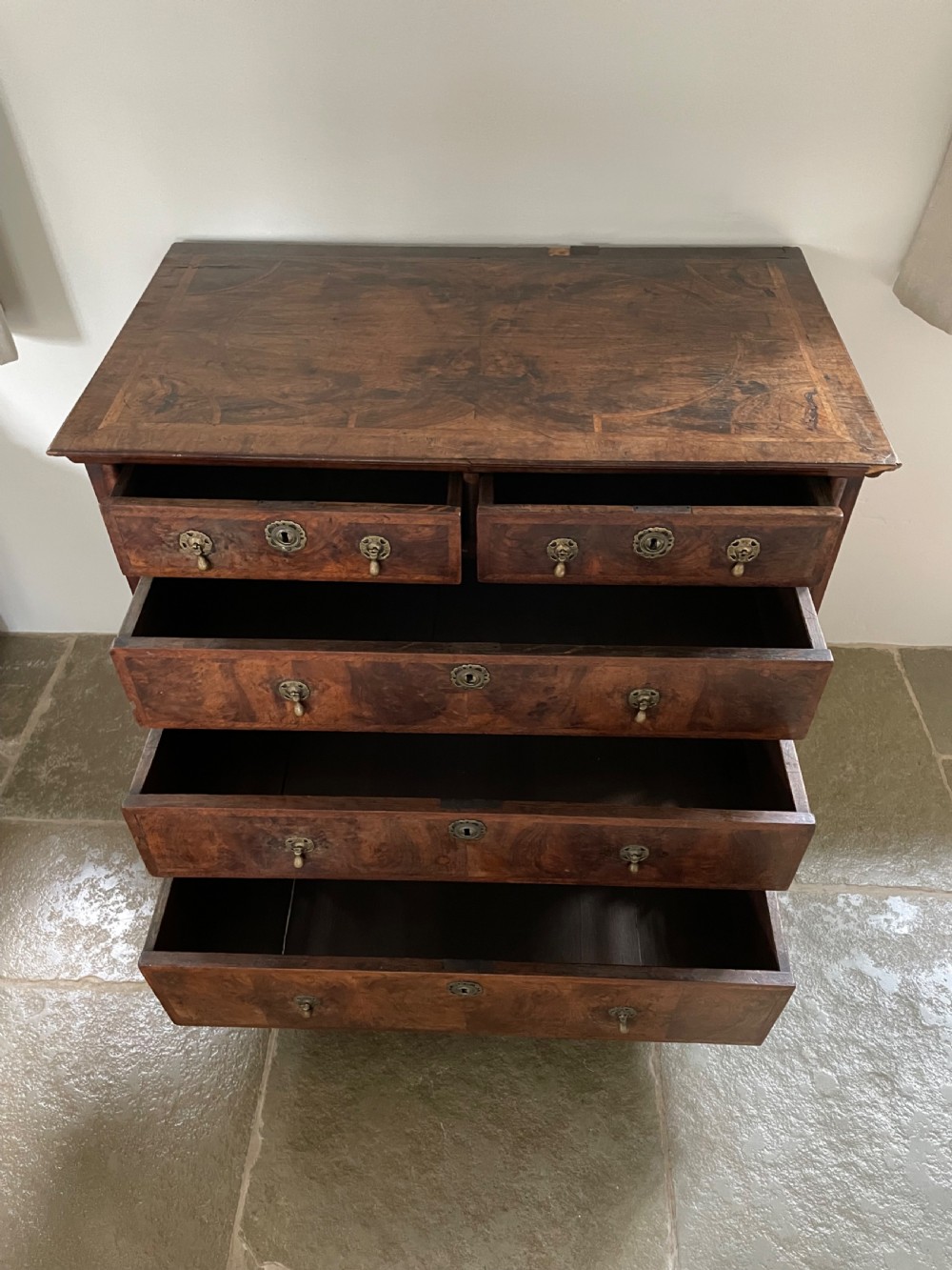 A late 17th-century walnut chest of drawers featuring brass teardrop handles, keyhole escutcheons, crossbanded veneer drawer fronts, and turned bun feet. View VI