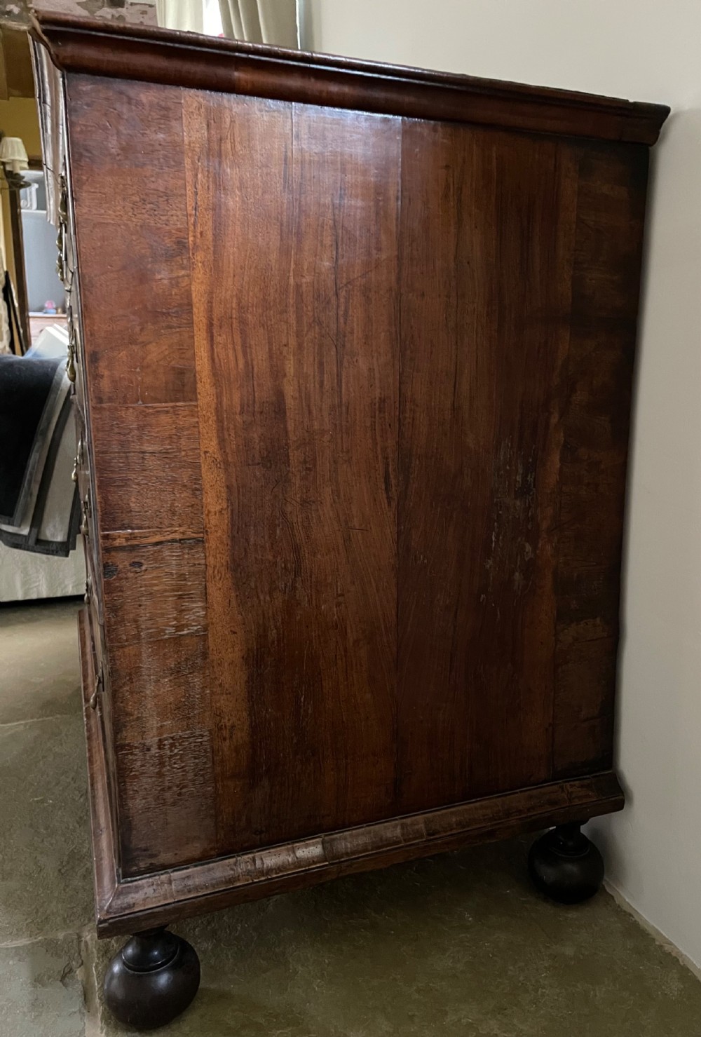 A late 17th-century walnut chest of drawers featuring brass teardrop handles, keyhole escutcheons, crossbanded veneer drawer fronts, and turned bun feet. View VII