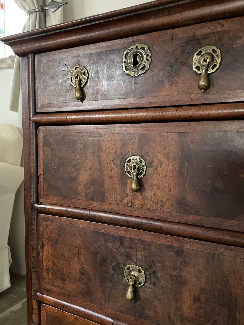 A late 17th-century walnut chest of drawers featuring brass teardrop handles, keyhole escutcheons, crossbanded veneer drawer fronts, and turned bun feet. View IX