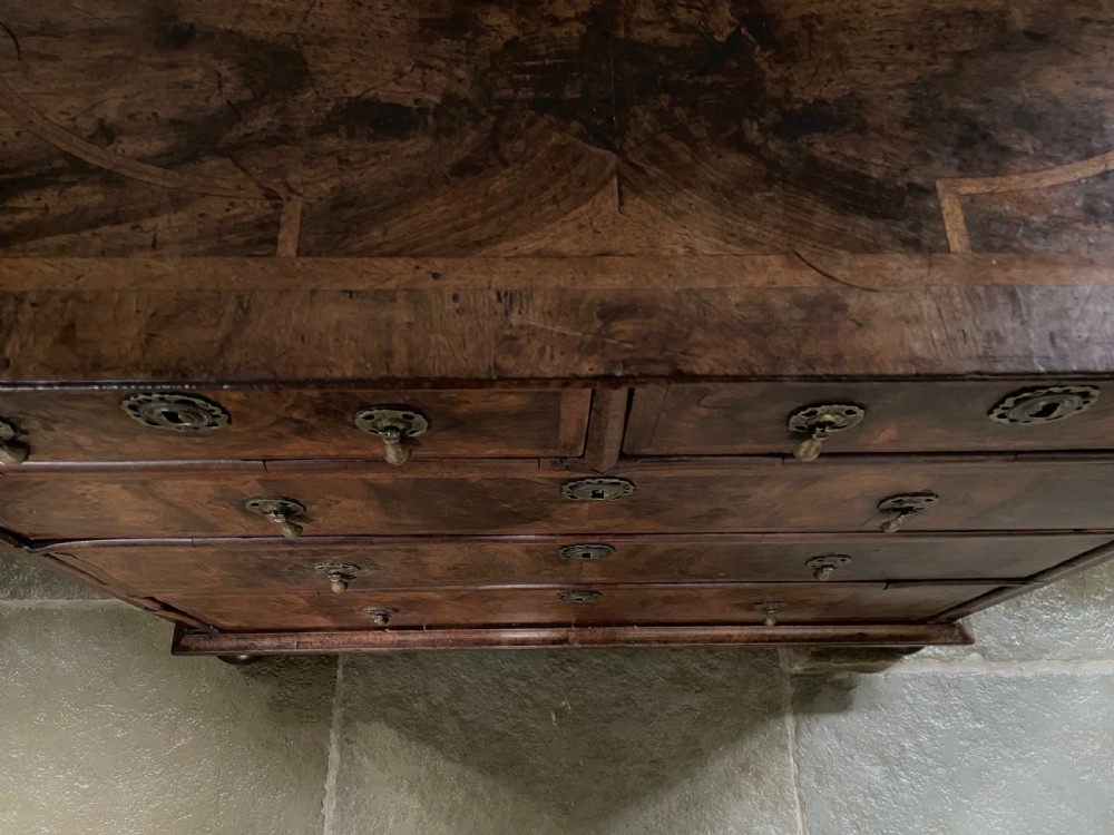 A late 17th-century walnut chest of drawers featuring brass teardrop handles, keyhole escutcheons, crossbanded veneer drawer fronts, and turned bun feet. View XIII