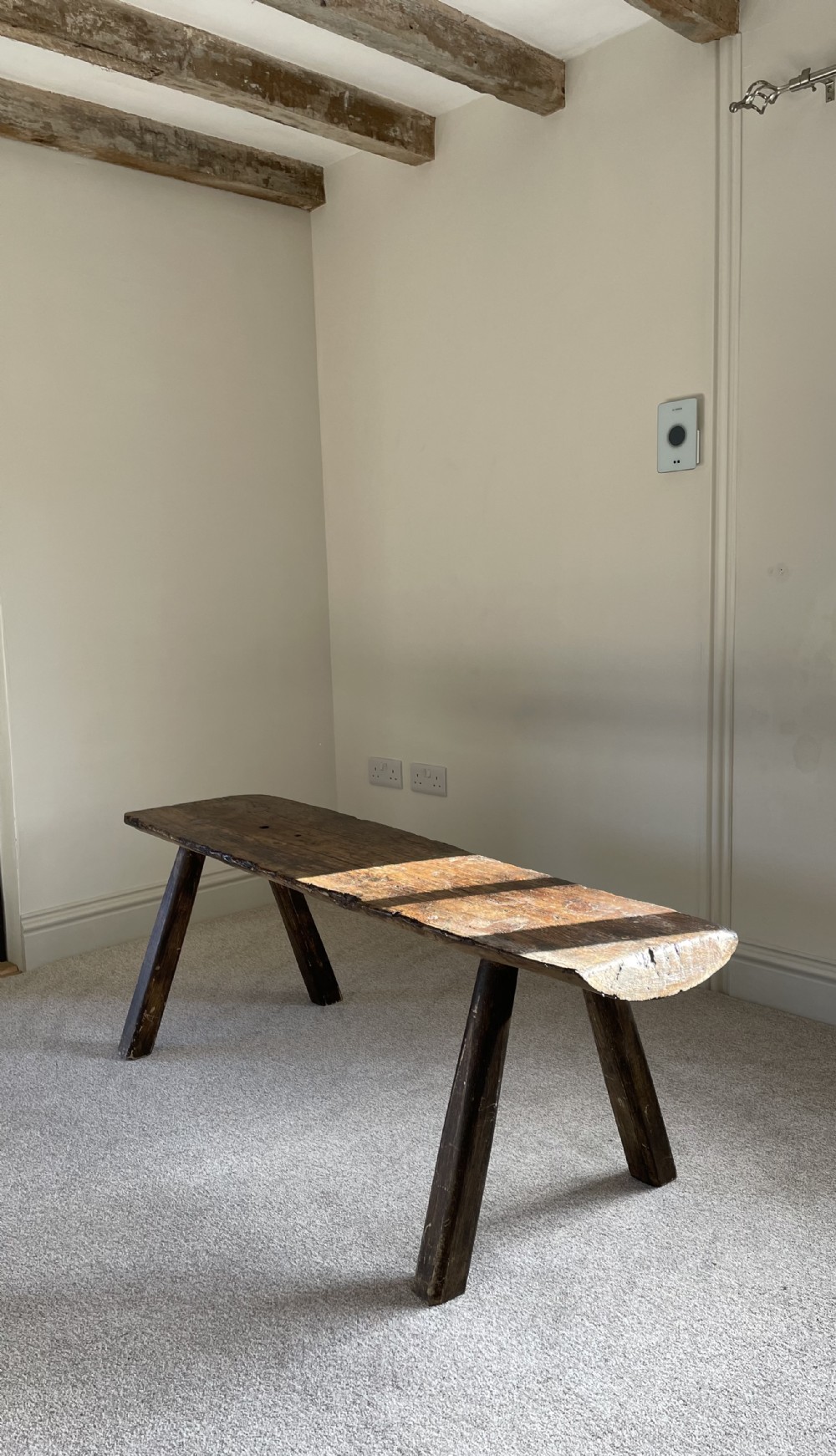 A primitive dark pine bench featuring a thick hand-carved timber seat supported by four splayed round legs.