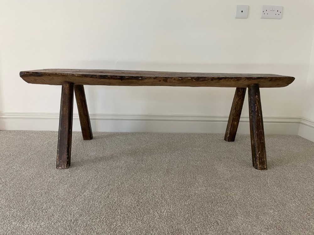 A primitive dark pine bench featuring a thick hand-carved timber seat supported by four splayed round legs. View II