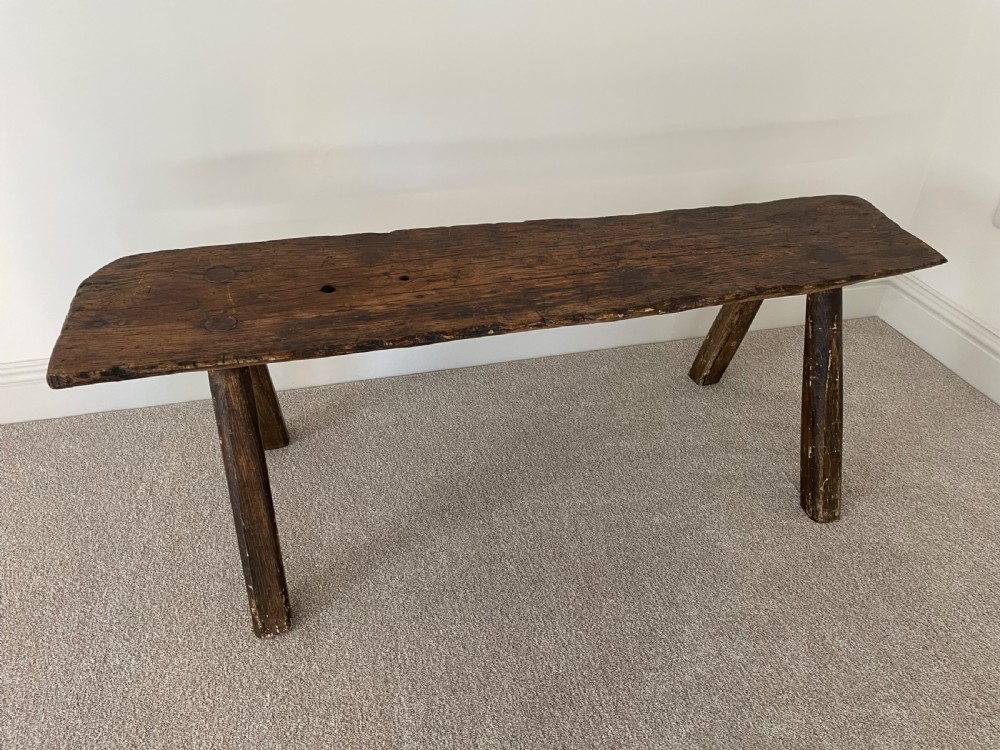 A primitive dark pine bench featuring a thick hand-carved timber seat supported by four splayed round legs. View III