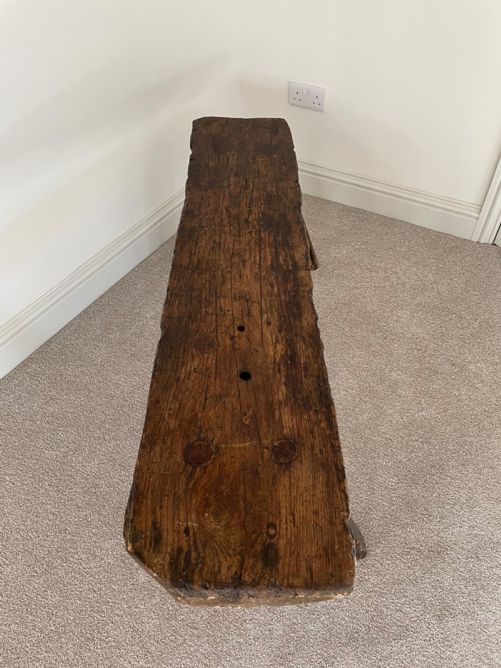 A primitive dark pine bench featuring a thick hand-carved timber seat supported by four splayed round legs. View IV
