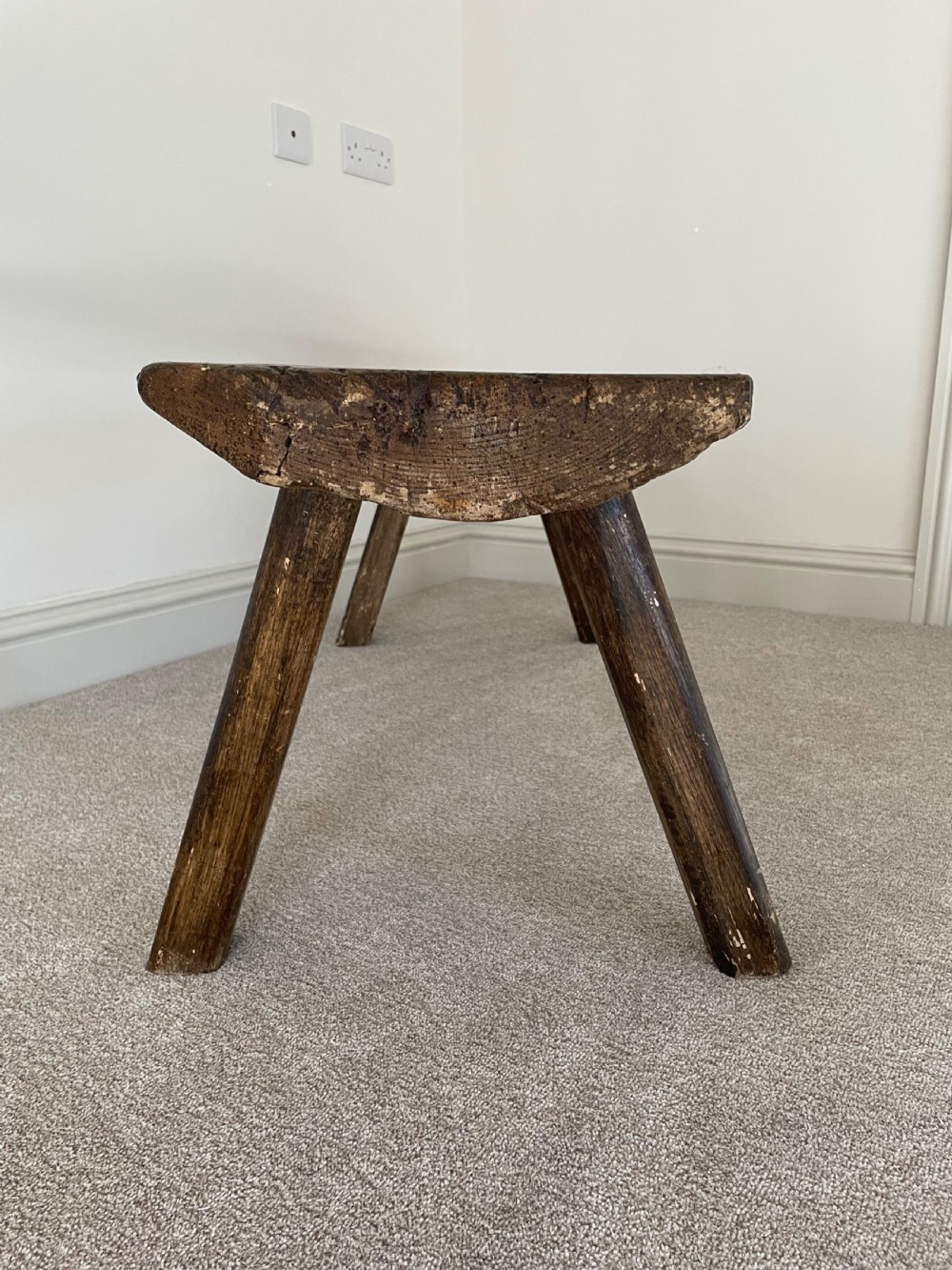 A primitive dark pine bench featuring a thick hand-carved timber seat supported by four splayed round legs. View V