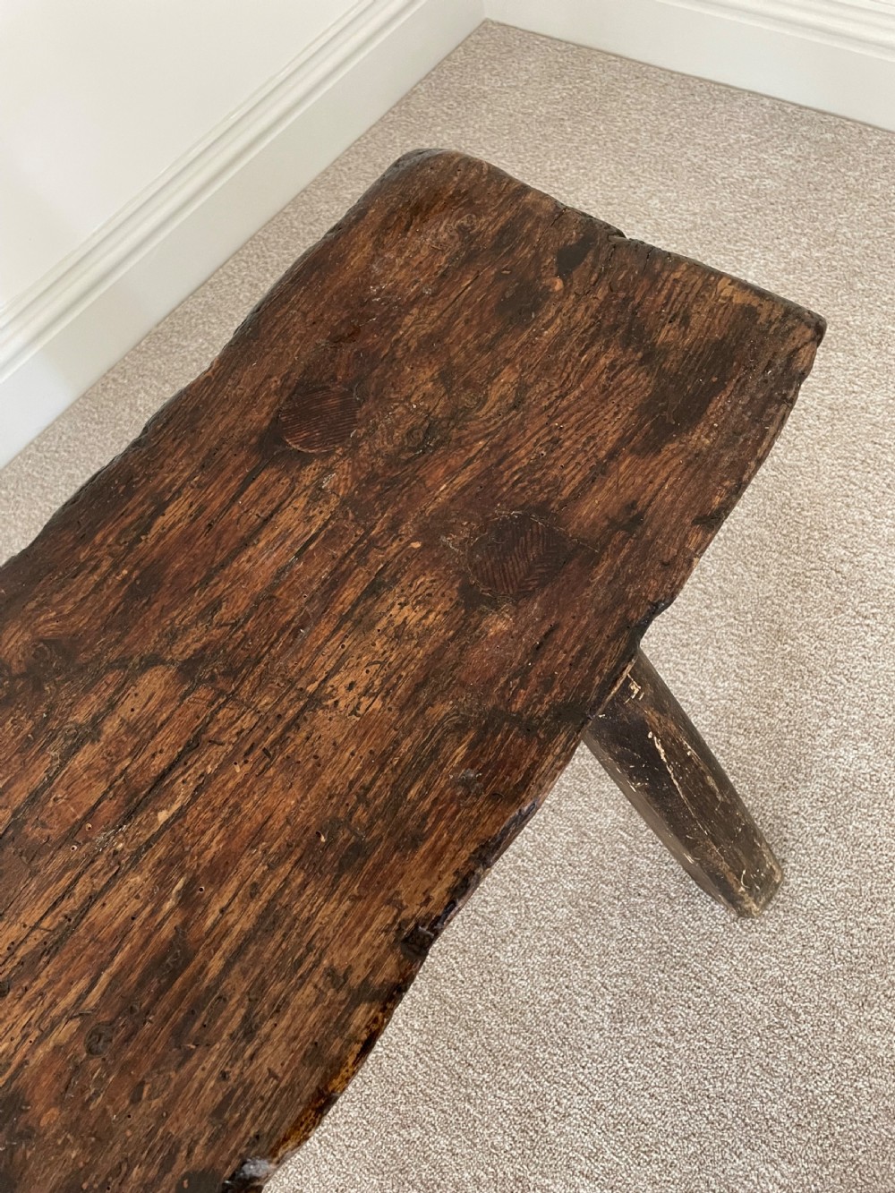 A primitive dark pine bench featuring a thick hand-carved timber seat supported by four splayed round legs. View VI
