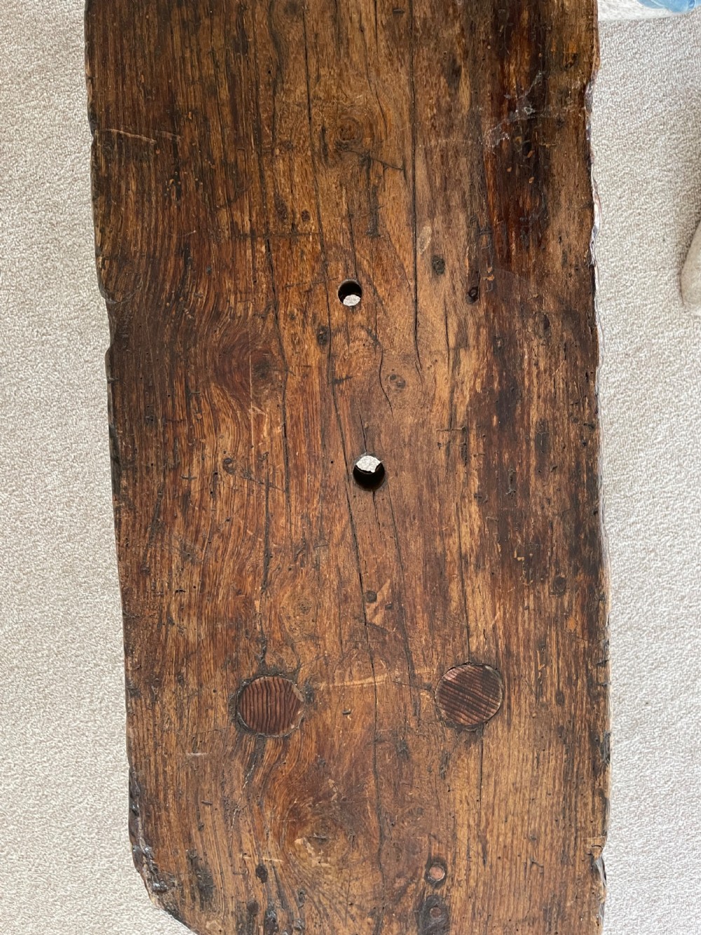 A primitive dark pine bench featuring a thick hand-carved timber seat supported by four splayed round legs. View VIII