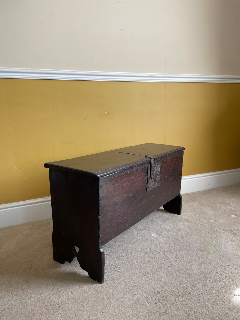 A dark 17th-century Jacobean oak six-plank coffer featuring a hinged lid, iron lockplate, and V-cut slab end supports.