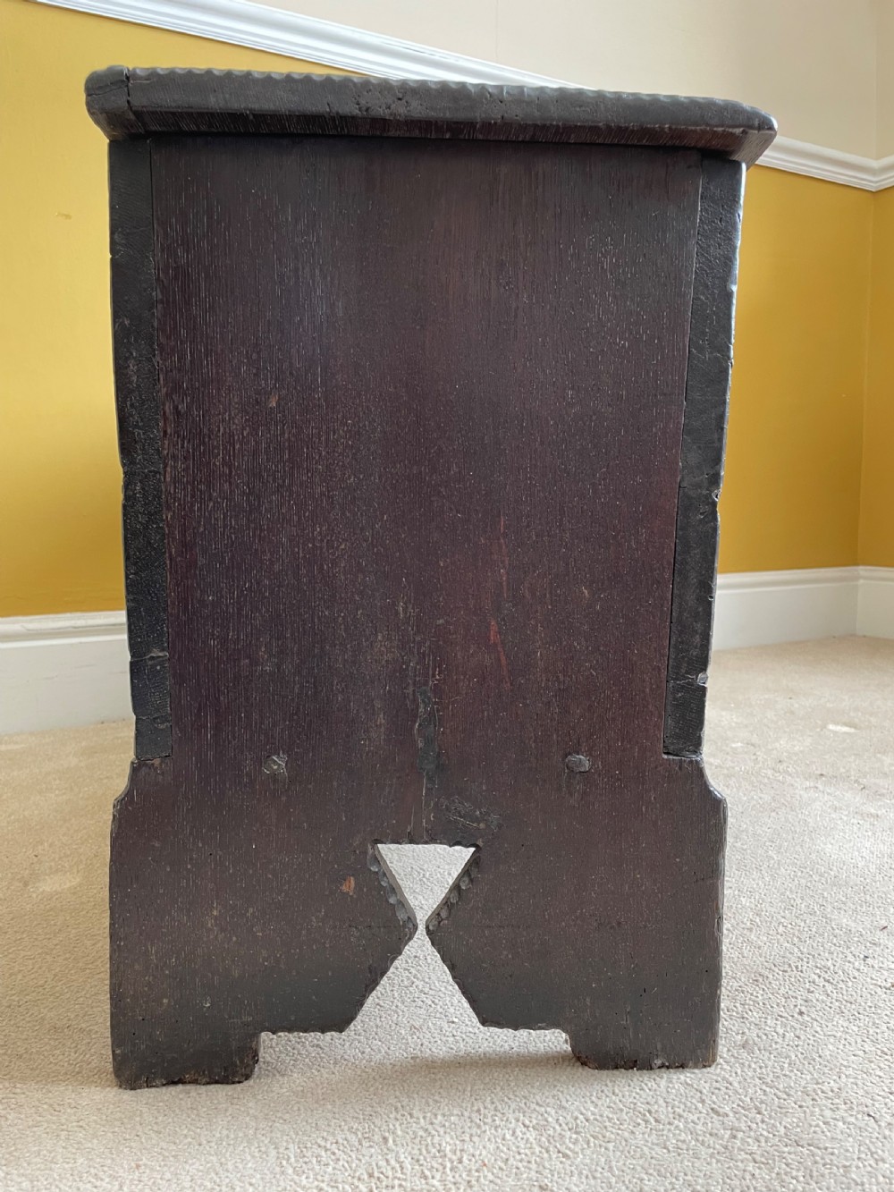 A dark 17th-century Jacobean oak six-plank coffer featuring a hinged lid, iron lockplate, and V-cut slab end supports. View V
