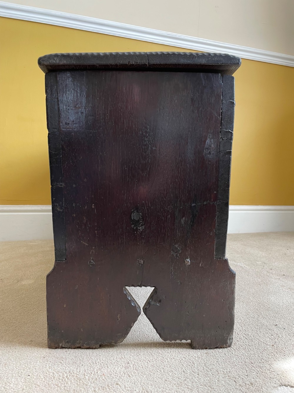 A dark 17th-century Jacobean oak six-plank coffer featuring a hinged lid, iron lockplate, and V-cut slab end supports. View VI