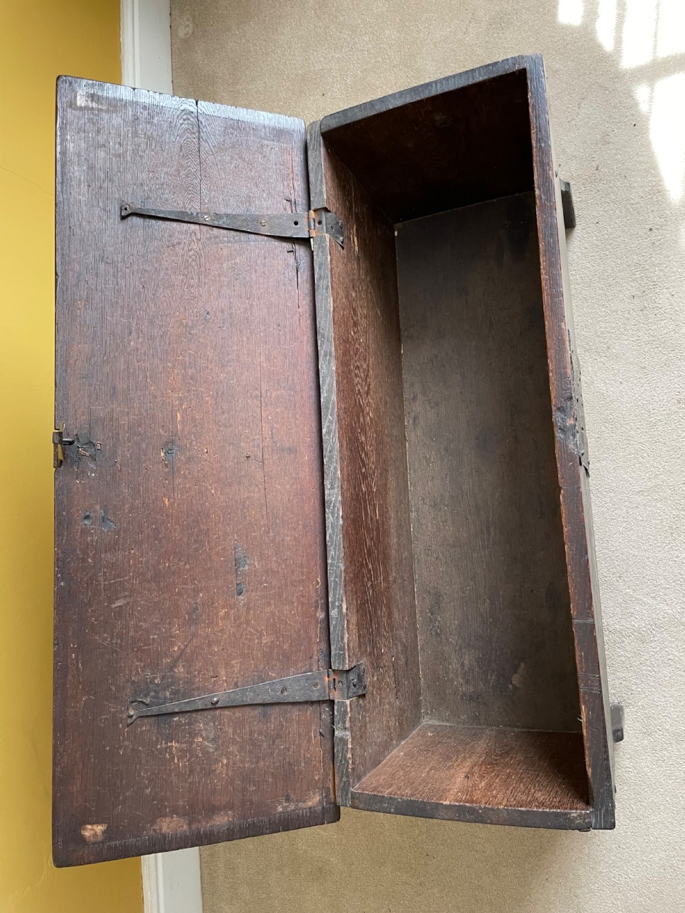 A dark 17th-century Jacobean oak six-plank coffer featuring a hinged lid, iron lockplate, and V-cut slab end supports. View VIII