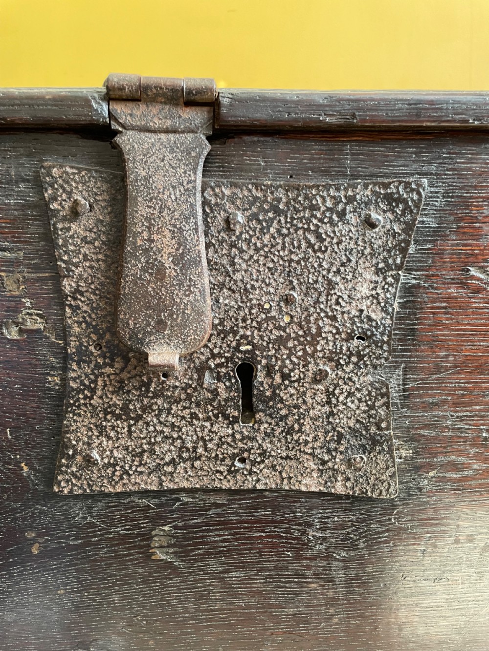 A dark 17th-century Jacobean oak six-plank coffer featuring a hinged lid, iron lockplate, and V-cut slab end supports. View X