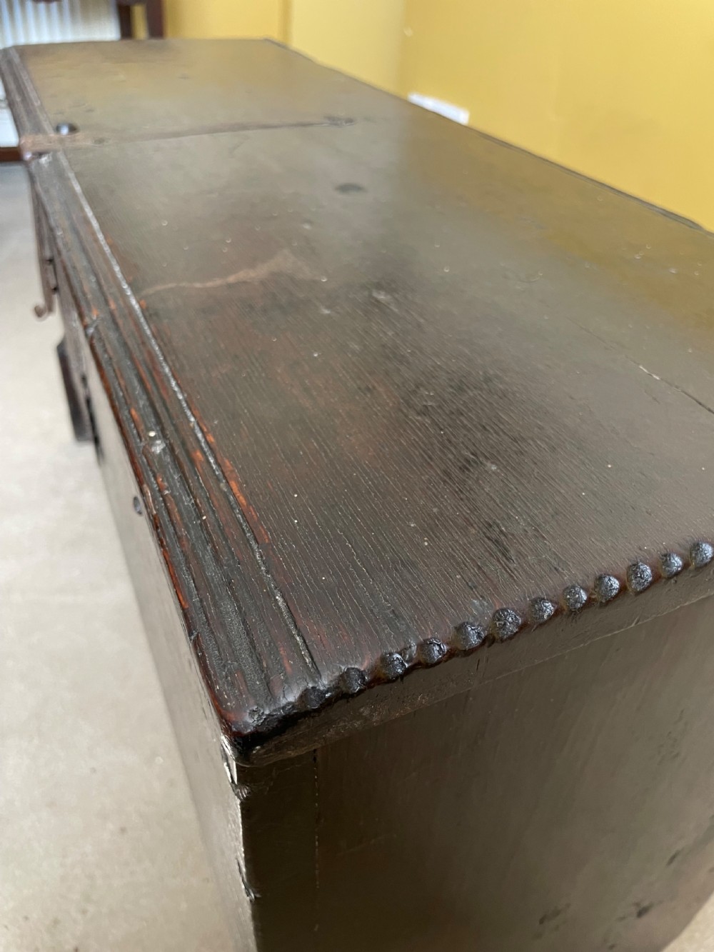 A dark 17th-century Jacobean oak six-plank coffer featuring a hinged lid, iron lockplate, and V-cut slab end supports. View XI