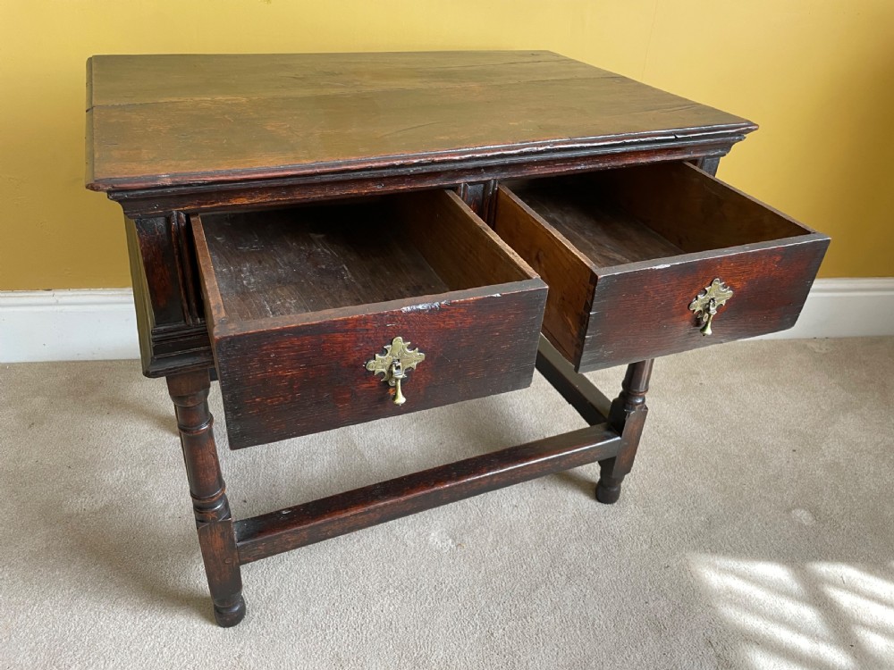A 17th-century dark oak rent table featuring two frieze drawers with decorative brass handles, supported on turned legs with a rectangular perimeter stretcher. View IV