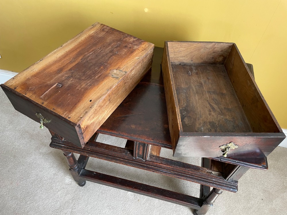 A 17th-century dark oak rent table featuring two frieze drawers with decorative brass handles, supported on turned legs with a rectangular perimeter stretcher. View XI