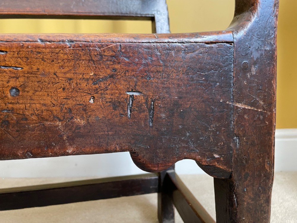 A dark oak Queen Anne period bench featuring open armrests, a vertical spindle backrest, a wooden plank seat, and a shaped apron. View V