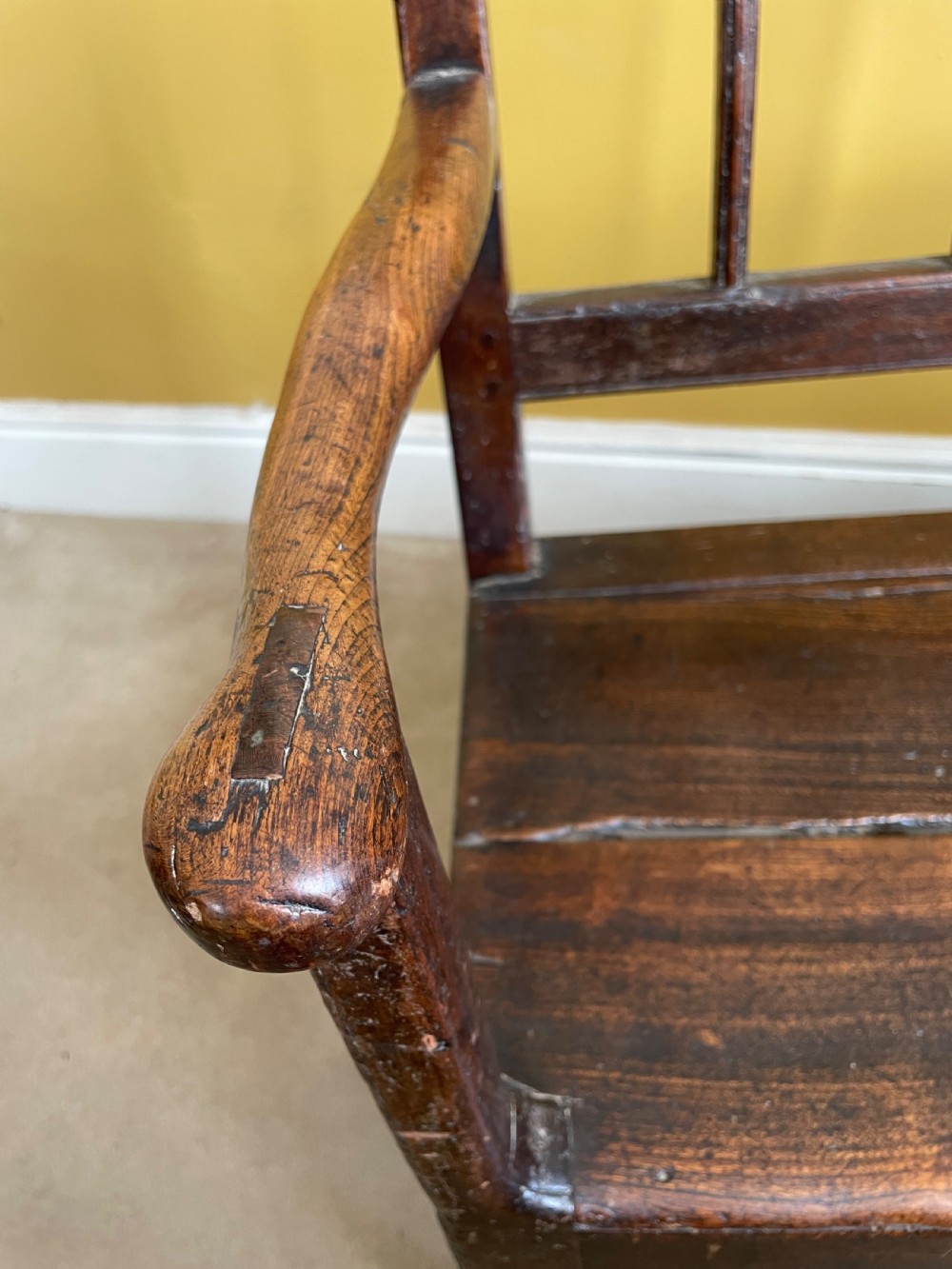 A dark oak Queen Anne period bench featuring open armrests, a vertical spindle backrest, a wooden plank seat, and a shaped apron. View VII