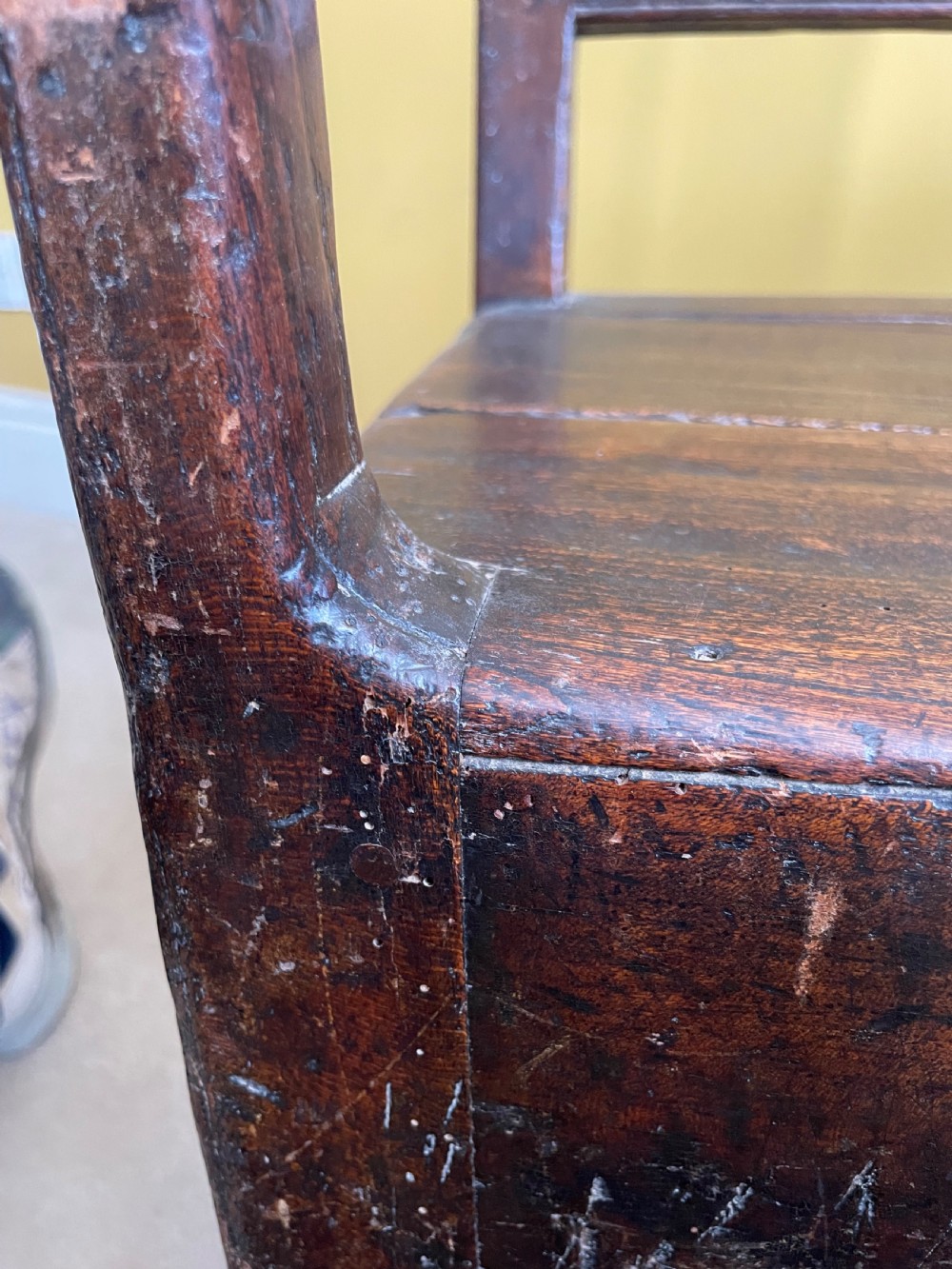 A dark oak Queen Anne period bench featuring open armrests, a vertical spindle backrest, a wooden plank seat, and a shaped apron. View XIII