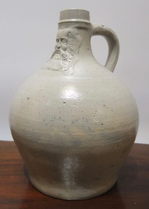 fig 1. A pale grey salt-glazed stoneware Bartmann jug with a rounded body and a moulded bearded face mask on the neck.