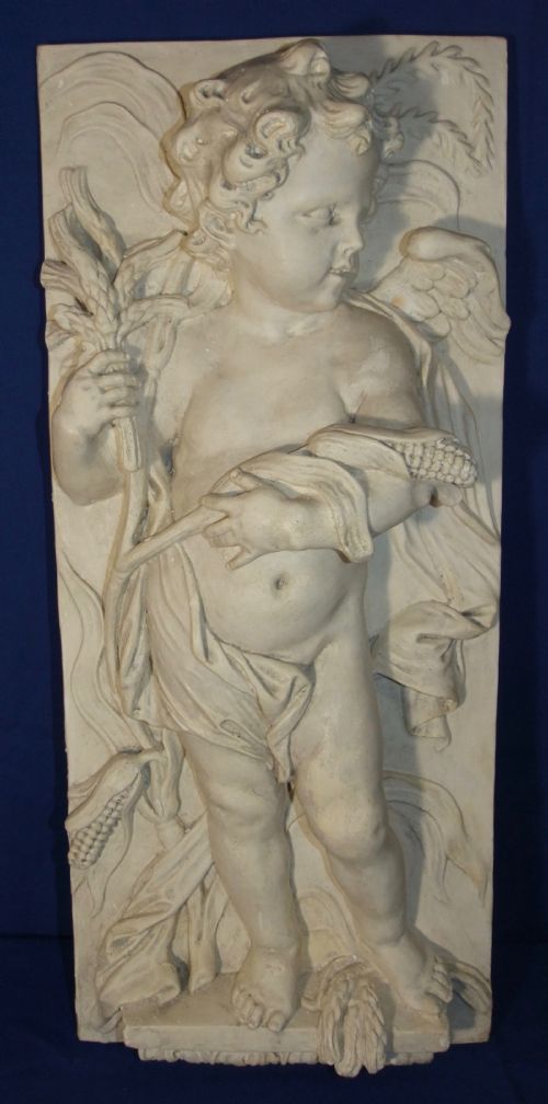 fig 1. A pair of vertical off-white plaster relief friezes depicting winged cherubs holding wheat sheaves and a chalice with grapes.