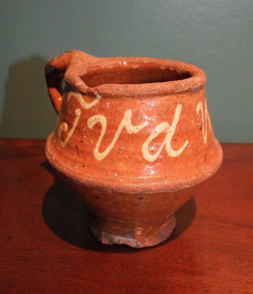 An antique Dutch slipware earthenware jar in terracotta red lead glaze featuring white trailed script lettering and a single handle.