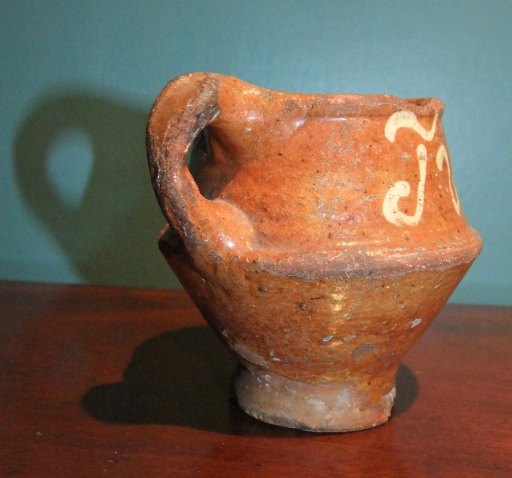 An antique Dutch slipware earthenware jar in terracotta red lead glaze featuring white trailed script lettering and a single handle. View IV