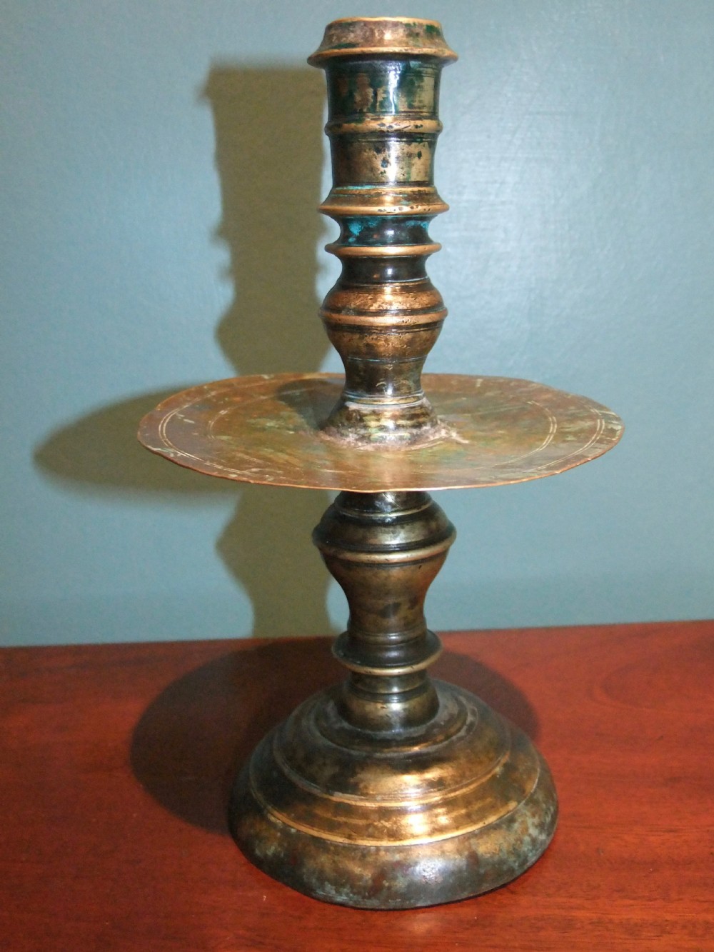 An 18th-century cast brass candlestick featuring a wide central drip collar, turned knopped stem, and a round stepped base.