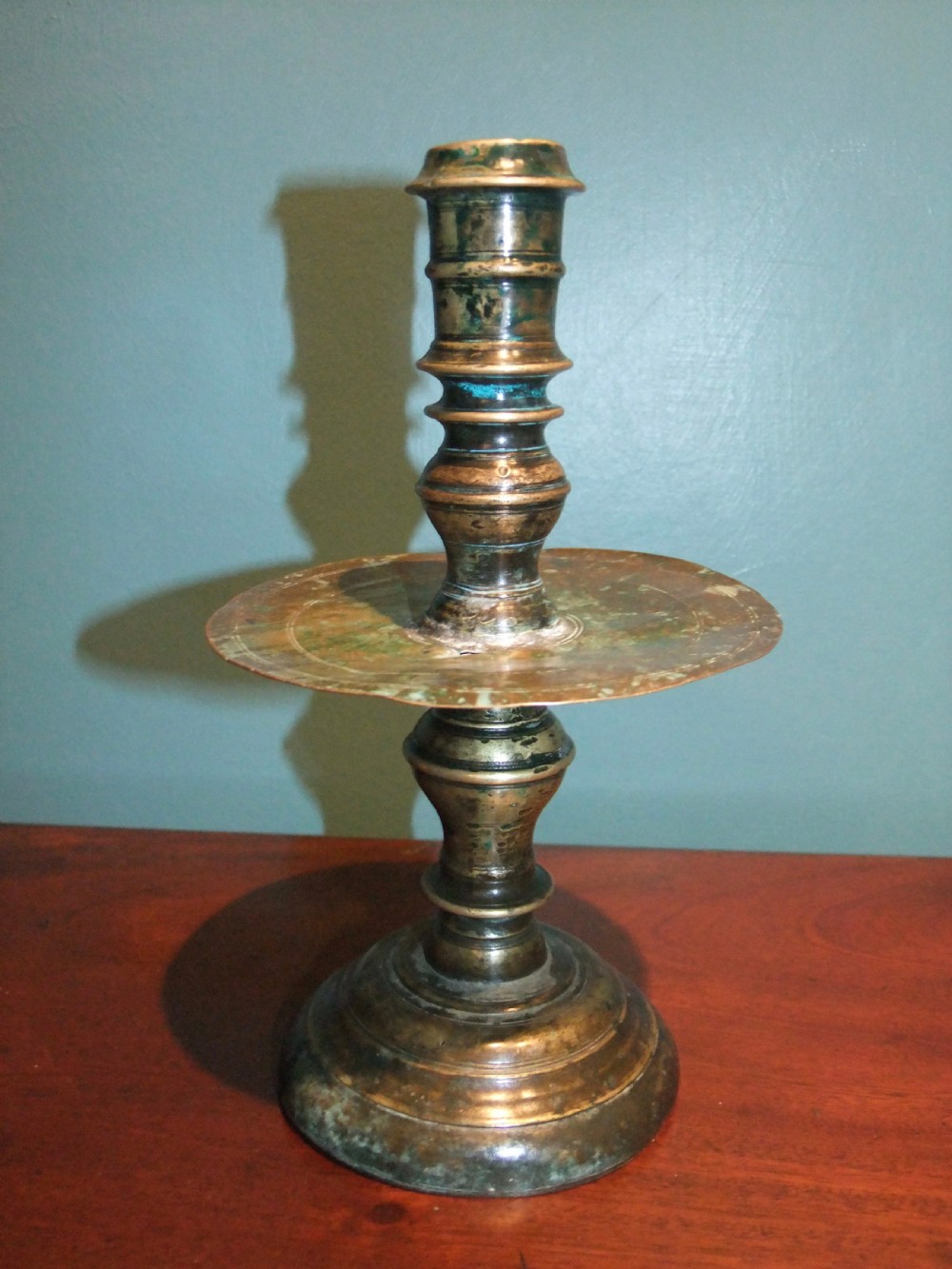 An 18th-century cast brass candlestick featuring a wide central drip collar, turned knopped stem, and a round stepped base. View II