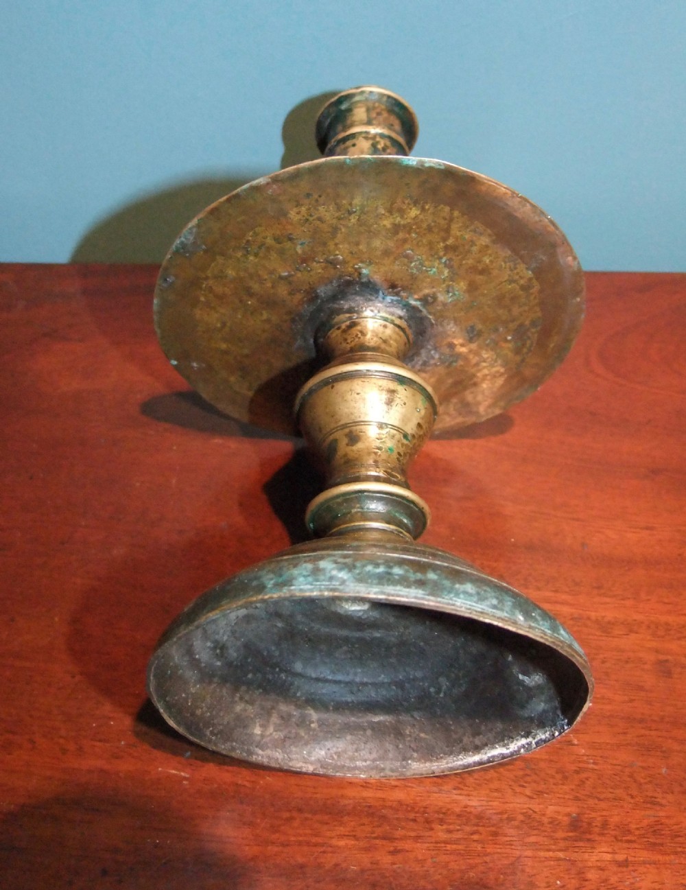 An 18th-century cast brass candlestick featuring a wide central drip collar, turned knopped stem, and a round stepped base. View V
