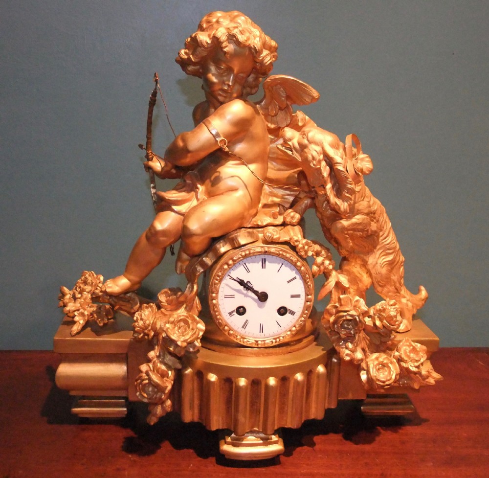A 19th-century French gilt bronze mantel clock featuring a sculpted putto figure with a bow alongside a dog atop an ornate base.