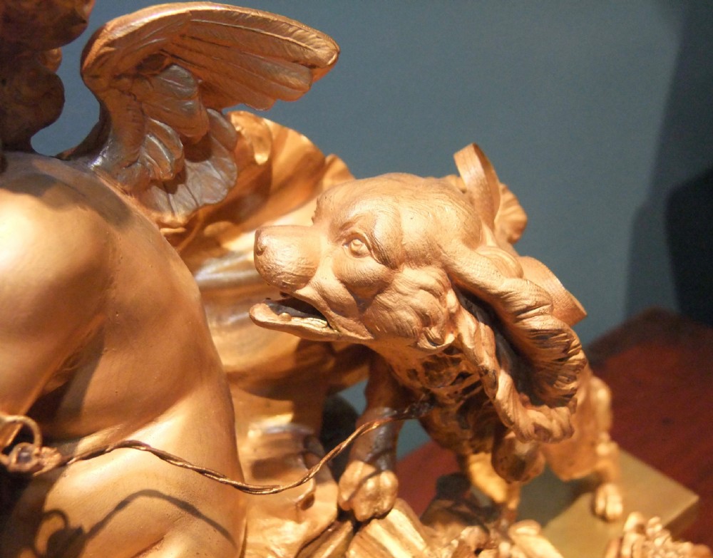A 19th-century French gilt bronze mantel clock featuring a sculpted putto figure with a bow alongside a dog atop an ornate base. View V