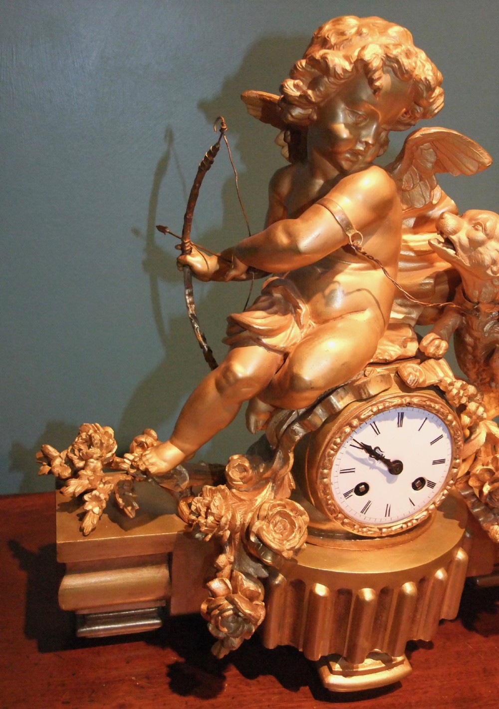A 19th-century French gilt bronze mantel clock featuring a sculpted putto figure with a bow alongside a dog atop an ornate base. View VI