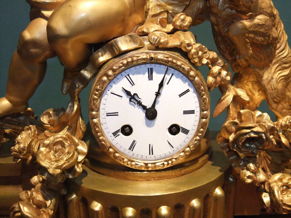 A 19th-century French gilt bronze mantel clock featuring a sculpted putto figure with a bow alongside a dog atop an ornate base. View VIII