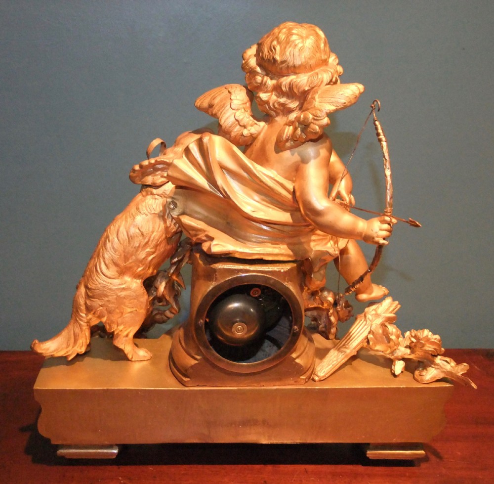 A 19th-century French gilt bronze mantel clock featuring a sculpted putto figure with a bow alongside a dog atop an ornate base. View IX