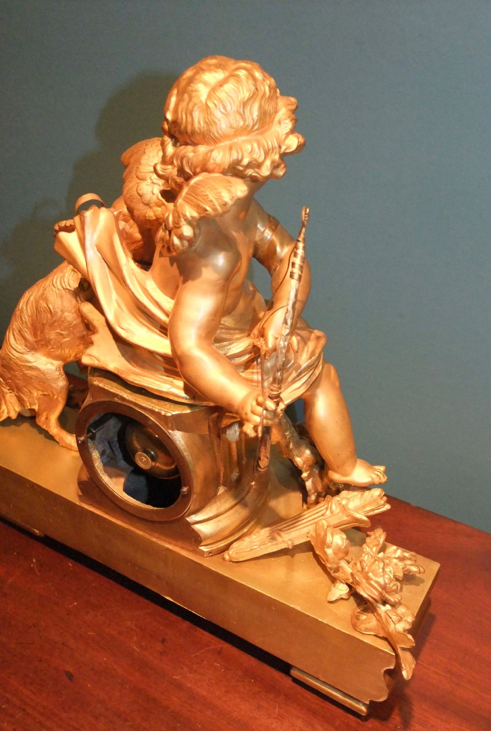 A 19th-century French gilt bronze mantel clock featuring a sculpted putto figure with a bow alongside a dog atop an ornate base. View X