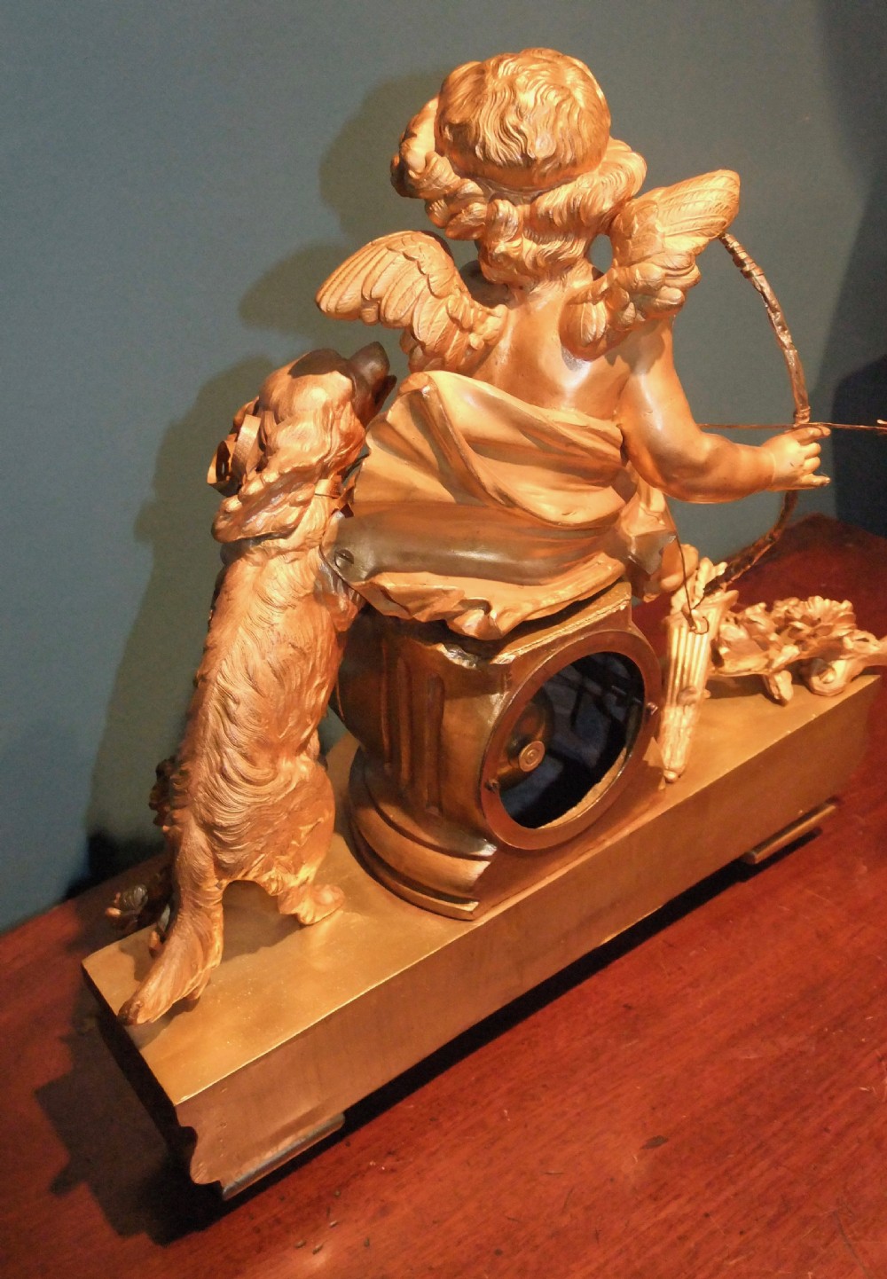 A 19th-century French gilt bronze mantel clock featuring a sculpted putto figure with a bow alongside a dog atop an ornate base. View XI