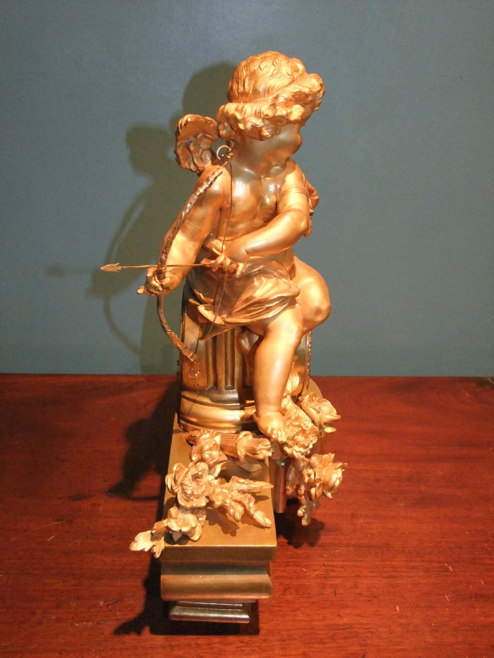 A 19th-century French gilt bronze mantel clock featuring a sculpted putto figure with a bow alongside a dog atop an ornate base. View XII