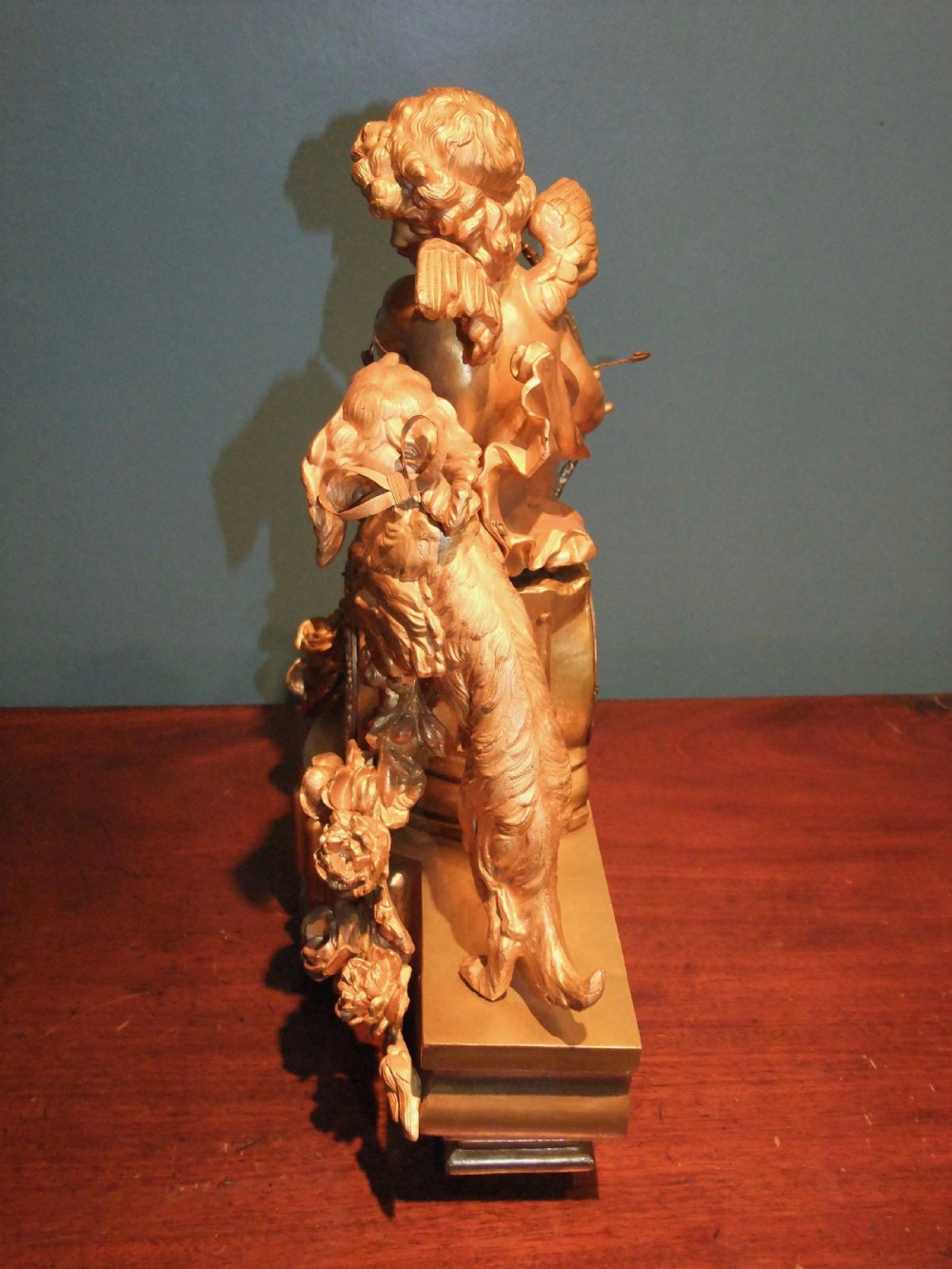 A 19th-century French gilt bronze mantel clock featuring a sculpted putto figure with a bow alongside a dog atop an ornate base. View XIII