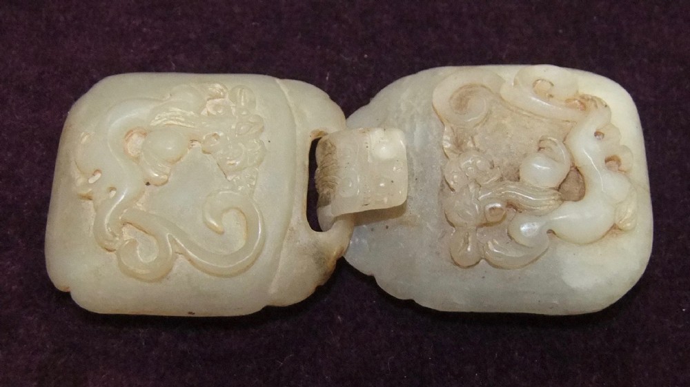 A two-part carved off-white jade belt buckle featuring raised dragon reliefs and an interlocking loop mechanism.