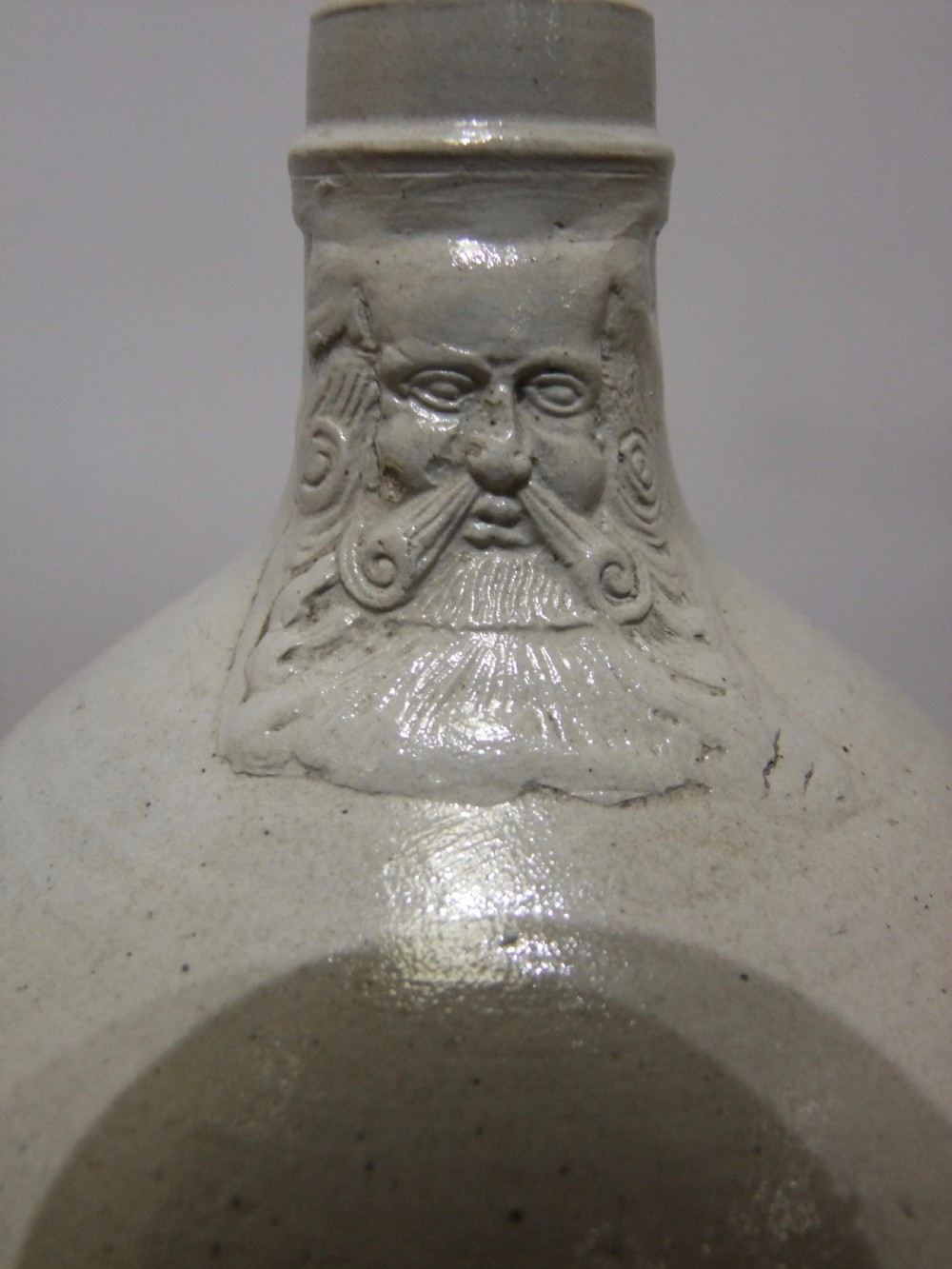 A pale grey salt-glazed stoneware Bartmann jug with a rounded body and a moulded bearded face mask on the neck. View V