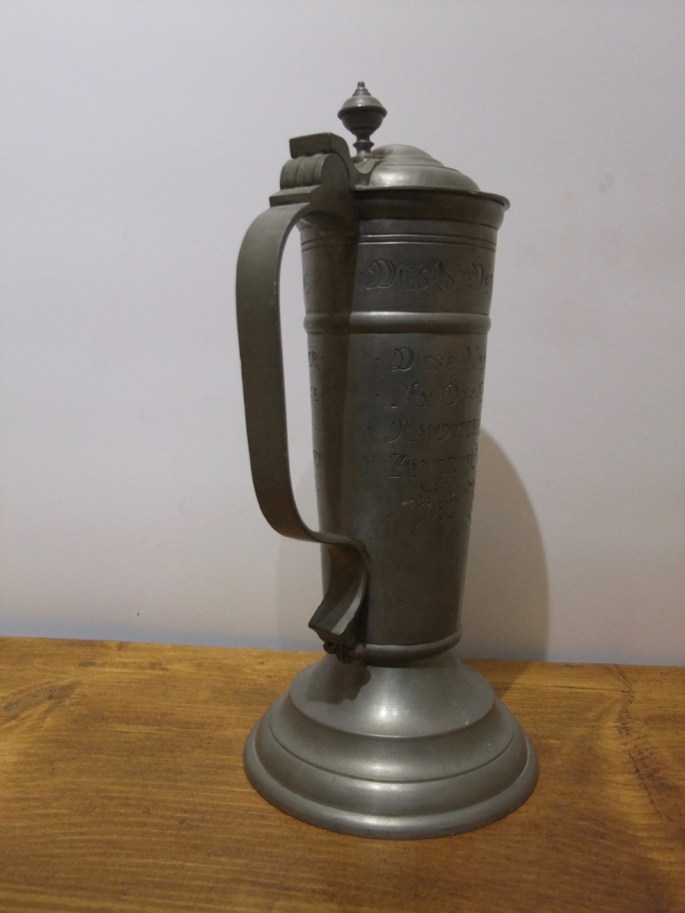 A tall 19th-century German lidded pewter tankard featuring hand-engraved Masonic iconography, floral sprigs, German text, a hinged lid with finial, and a flared pedestal base. View IV
