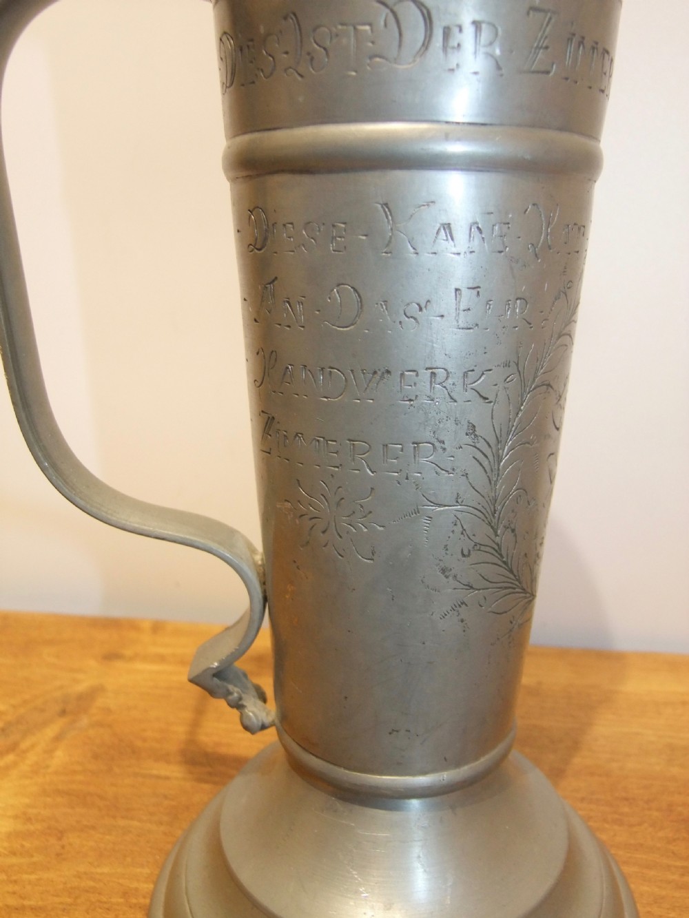 A tall 19th-century German lidded pewter tankard featuring hand-engraved Masonic iconography, floral sprigs, German text, a hinged lid with finial, and a flared pedestal base. View VII
