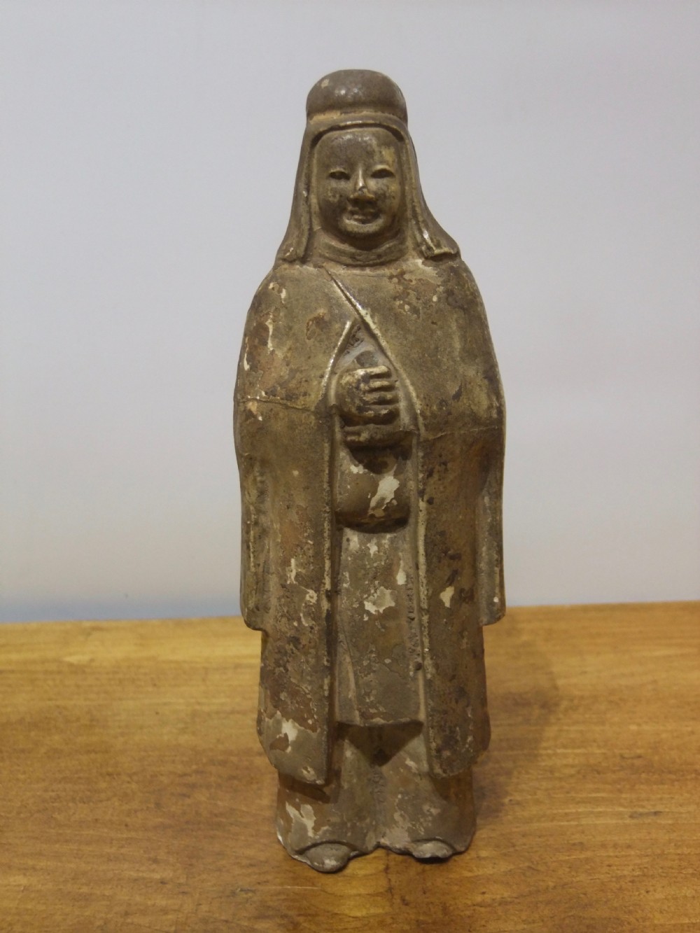 A standing Sui Dynasty earthenware tomb attendant figure featuring draped robes, a tall headpiece, folded hands, and traces of original surface pigments.