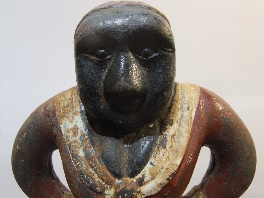 A nineteenth-century painted cast iron money bank depicting a standing figure with hands on hips wearing a red top and cream apron. View III