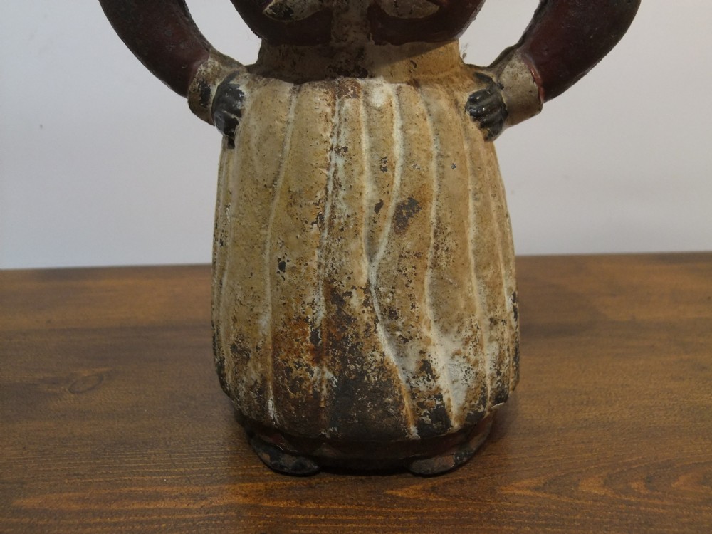 A nineteenth-century painted cast iron money bank depicting a standing figure with hands on hips wearing a red top and cream apron. View IV