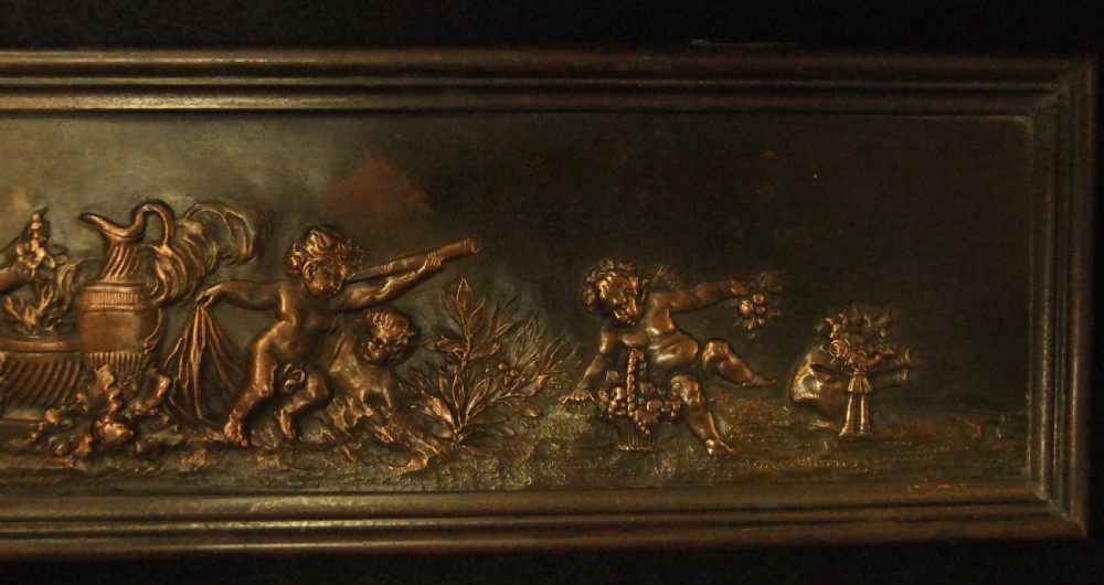 A long horizontal dark bronze relief frieze featuring classical cherubs engaged in allegorical scenes set within a slender rectangular frame. View V